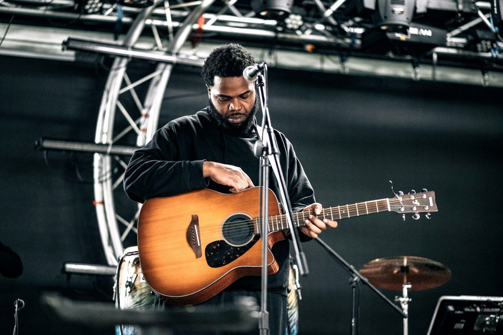 A musician playing an acoustic guitar on a lit concert stage